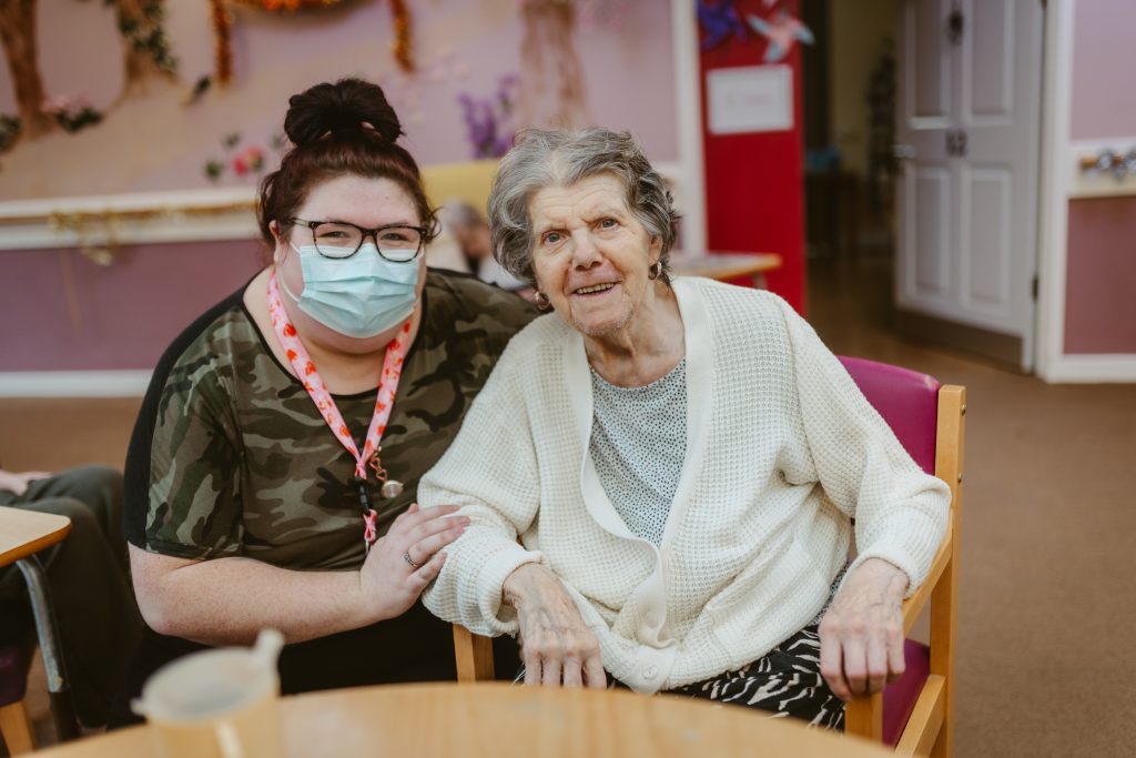 A female carer and resident smiling at the camera.