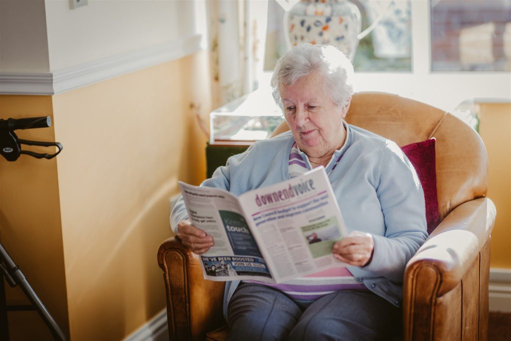 A woman reading a newspaper in the Woodland Court communal room.