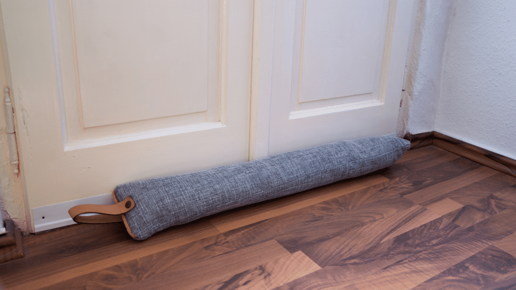 A grey draught excluder blocking a white door.