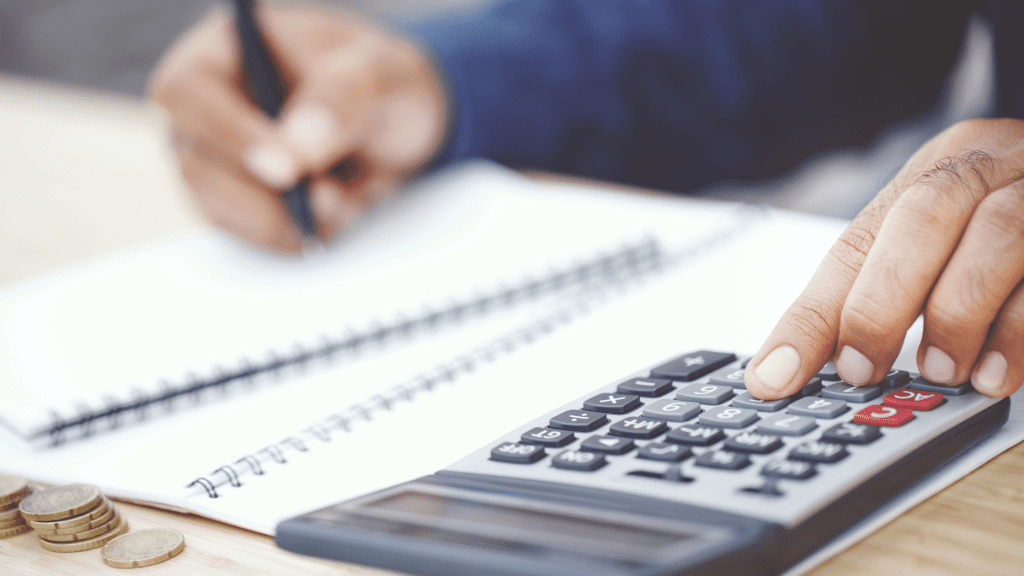 A pair of hands typing on a calculator and making notes.