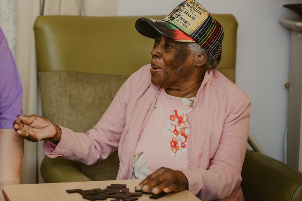 A female resident wearing a baseball cap plays dominos with a carer.